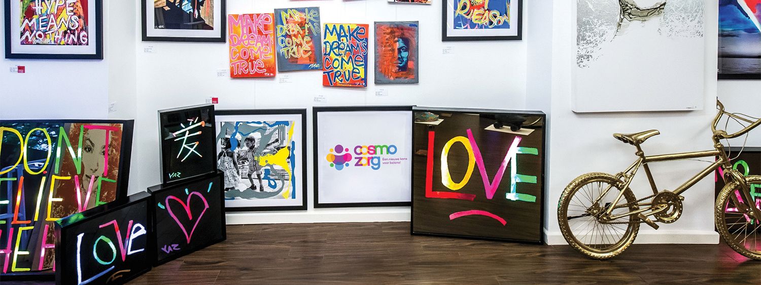 De galerieruimte van Cosmo Zorg: een muur vol ingelijste schilderijen van jongeren, met LOVE-doeken, MAKE DREAMS COME TRUE-posters en een goudkleurige BMX.